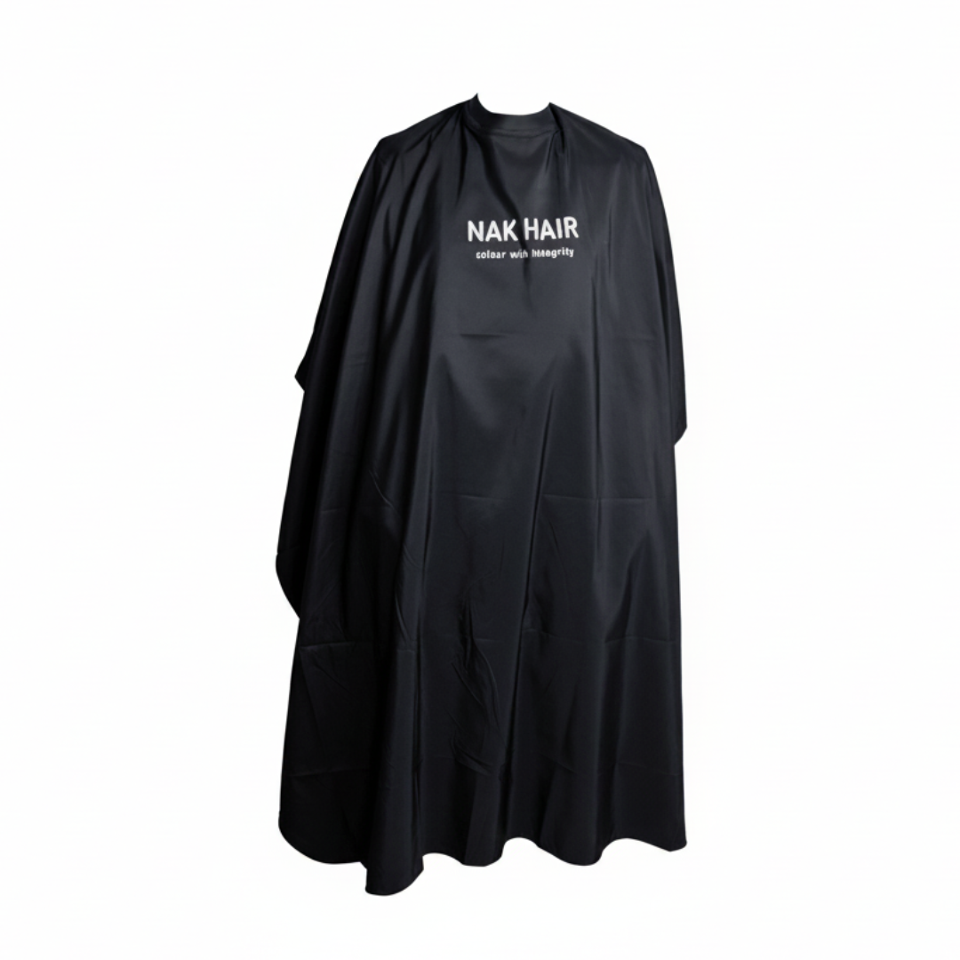 A black salon cape with 'NAK HAIR' printed in white on the chest, displayed against a solid pale pink background.